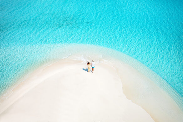 A holiday couple stands on a sandbar beach with turquoise, clear water Viajar en temporada alta
